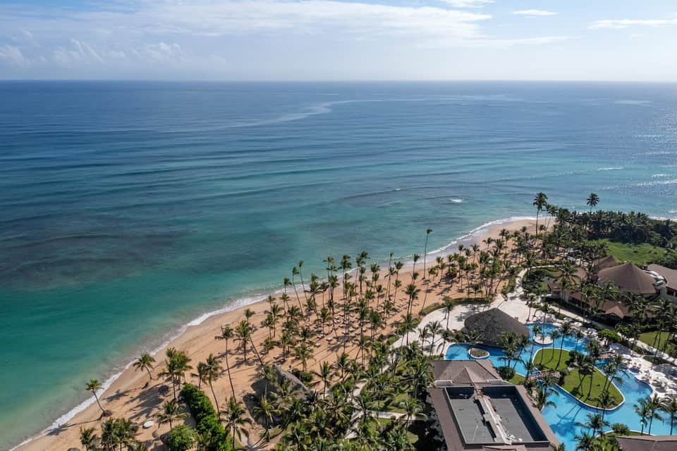 Aerial beachfront resort with turquoise pools, palm trees, sandy beach, and ocean view