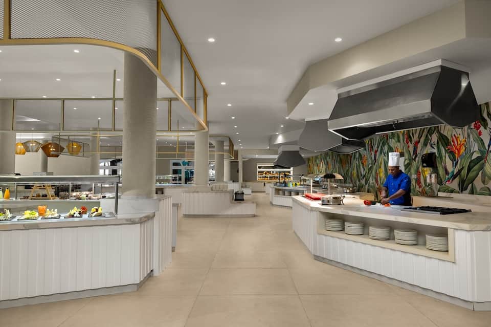 Modern hotel restaurant with white counters, botanical wallpaper, pendant lights, and open kitchen