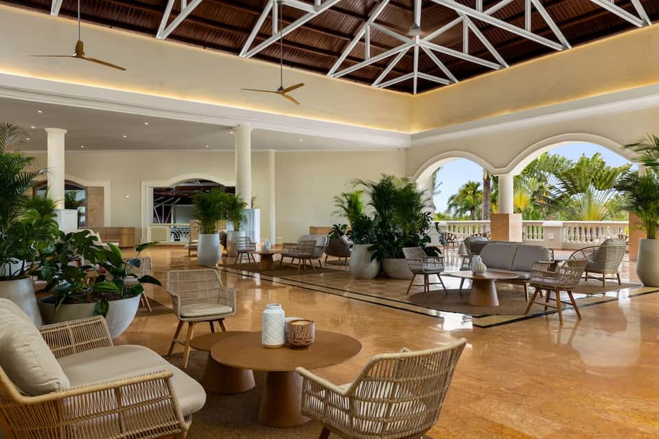 Elegant hotel lobby lounge with high ceilings, woven chairs, potted plants, and ocean views