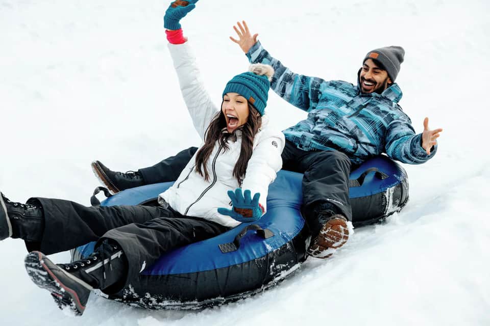 Couple sledding together down snowy slope in winter clothing with excited expressions