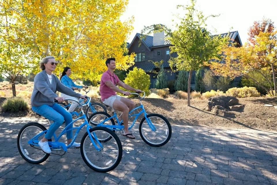 Resort guests cycling on blue bikes along paved path with fall foliage and house backdrop