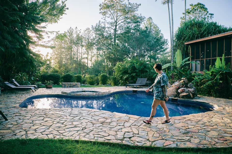 Guest jogging past curved resort pool surrounded by pine trees and stone patio