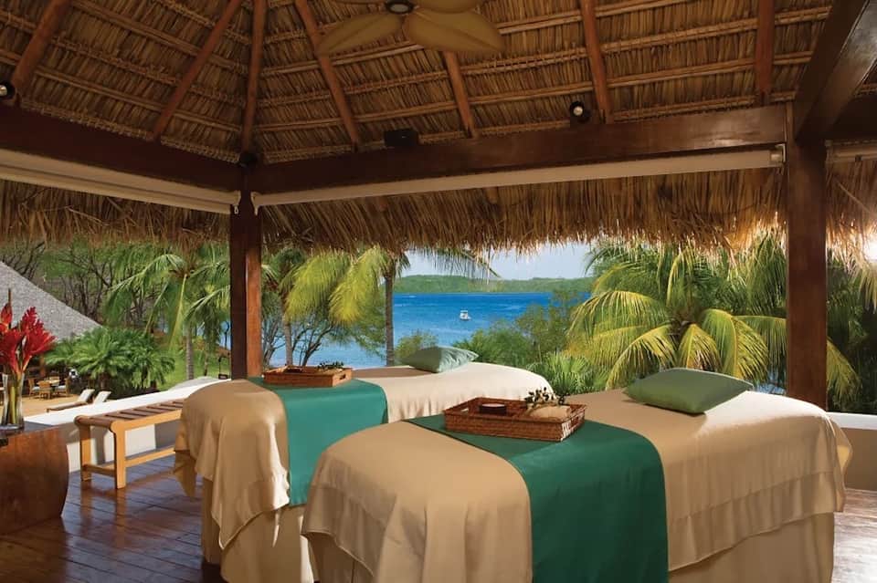 Tropical spa treatment room with thatched roof, ocean view, and massage tables