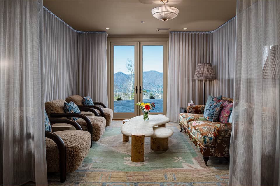 Luxury lounge with mountain and water views through French doors, upholstered seating, and sheer curtains