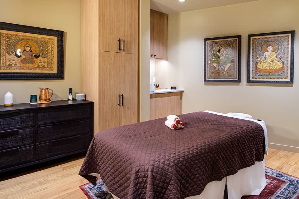 Spa treatment room with massage table, wooden cabinetry, decorative artwork, and warm lighting