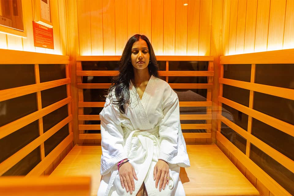 Woman in white robe relaxing in wooden infrared sauna with orange lighting