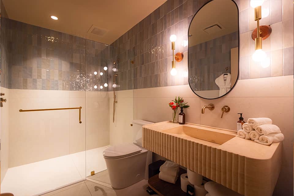 Modern bathroom with pink tile, dual sink vanity, walk-in shower, and brass fixtures