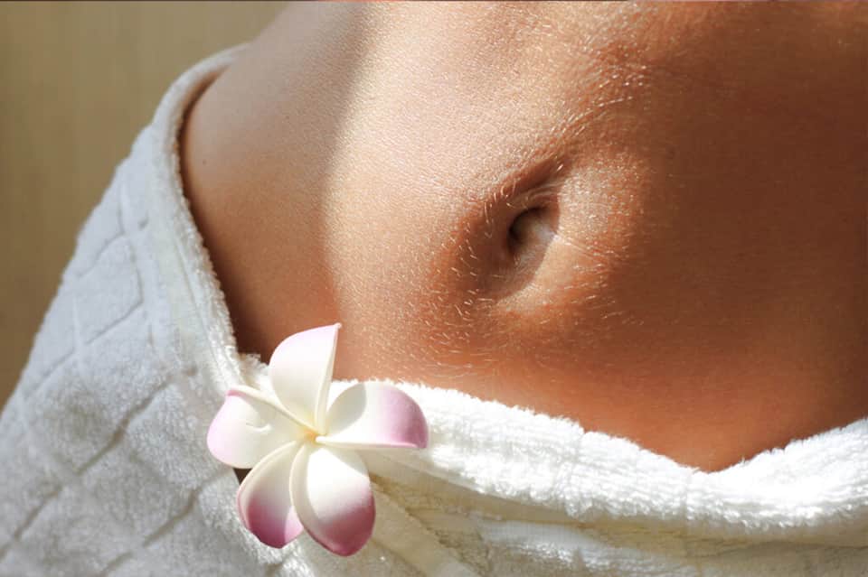 Spa setting showing person wrapped in white towel with plumeria flower accent