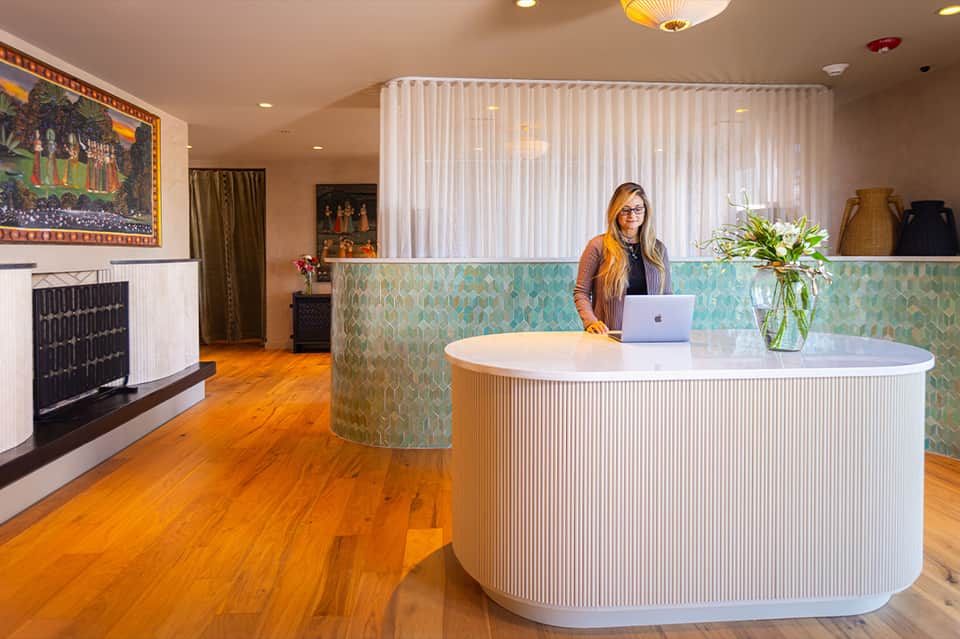 Hotel reception desk with curved design, turquoise patterned paneling, and warm wood flooring