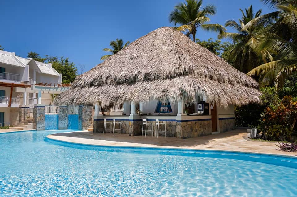Resort pool bar with large thatched-roof palapa structure and turquoise pool water