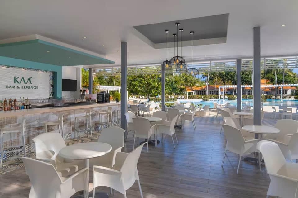 Modern bar and lounge area overlooking resort pool, white contemporary furniture, turquoise accent bar