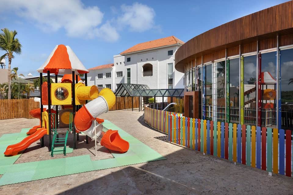 Children's playground with bright orange climbing structure, yellow tunnels, slides, and colorful fence