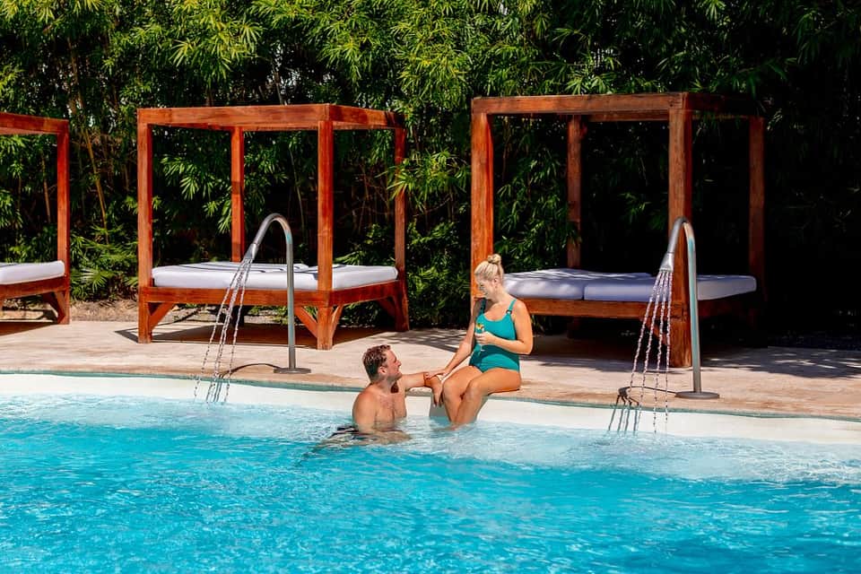 Couple relaxing in resort pool with wooden cabanas and bamboo backdrop