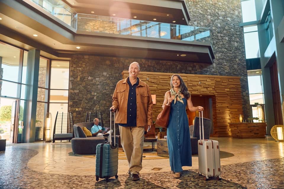 Hotel lobby with couple arriving with luggage, stone accent wall, wooden features, and modern architecture