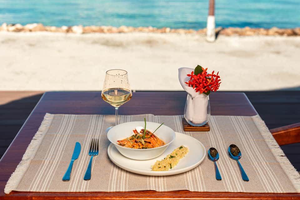 Beachfront dining setup with wine glass, plated food, flowers, and ocean view