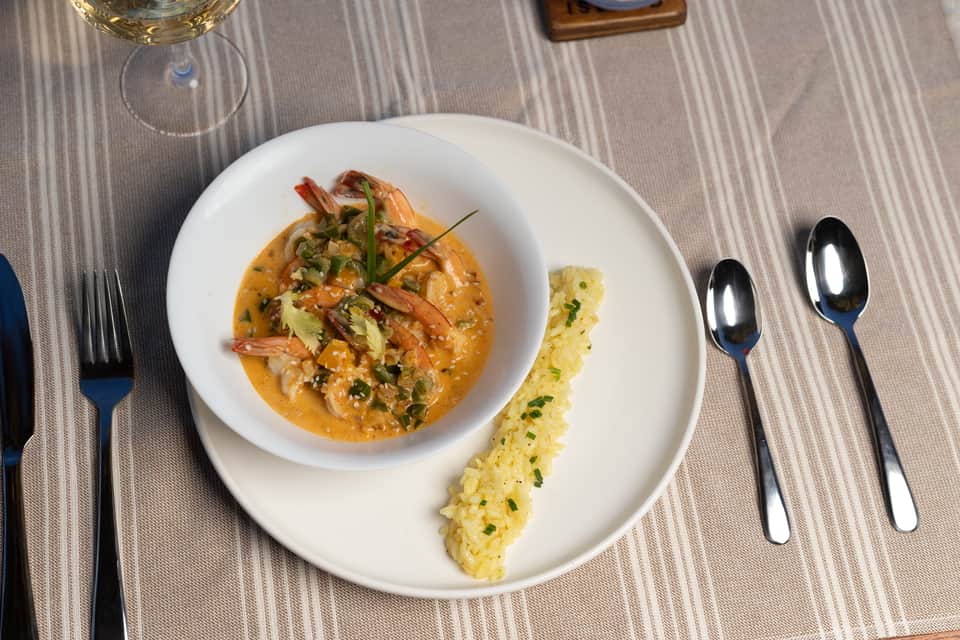 Fine dining plated seafood dish with shrimp and sauce accompanied by white wine