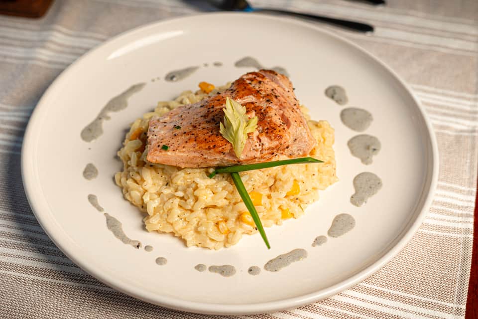 Gourmet plated salmon dish with risotto, green garnish, and decorative sauce dots on white plate