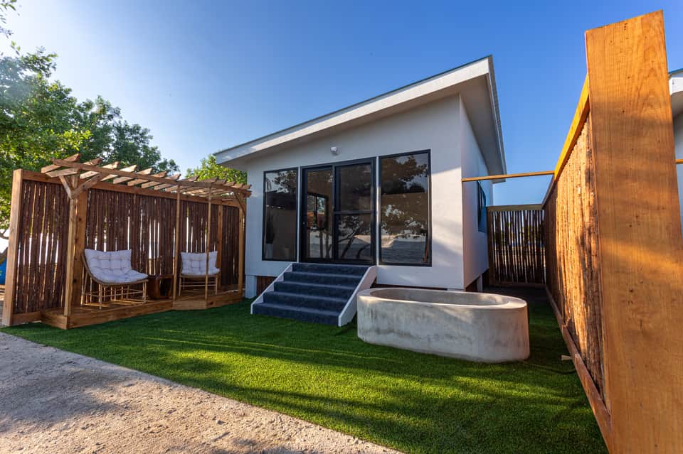 Glamping pod exterior with wooden pergola, white hanging chair, green lawn, and modern architecture