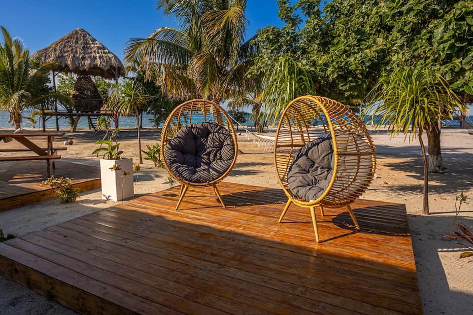 Beach lounge area with woven egg-shaped chairs, palm trees, thatched umbrellas, and tropical ocean view