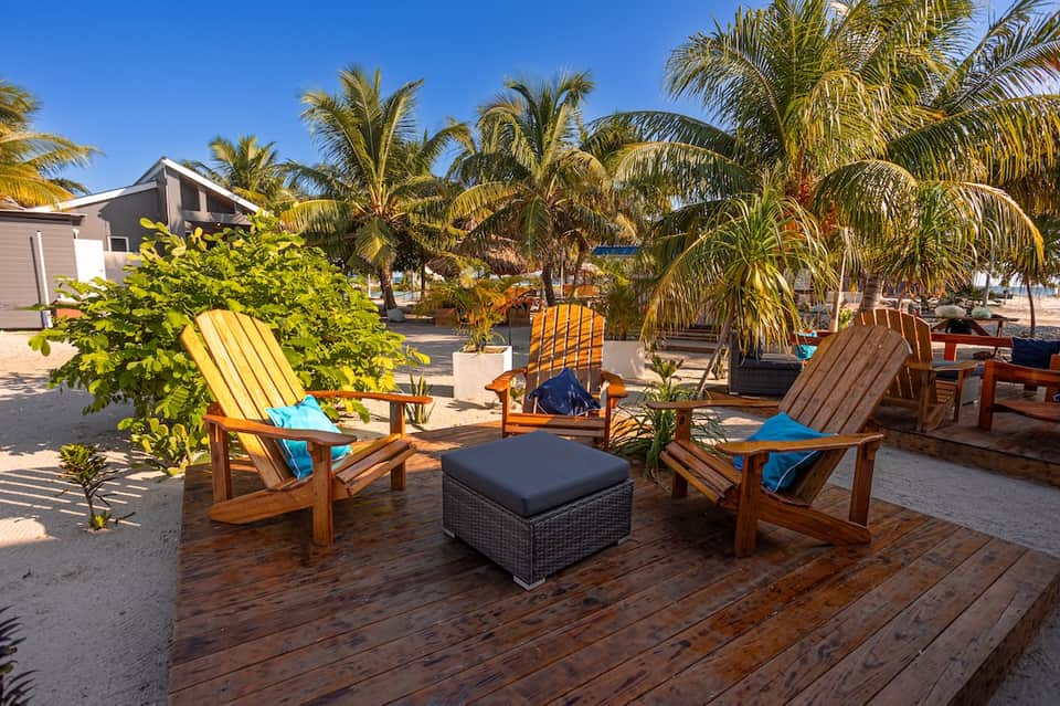 Beachside resort lounge area with colorful Adirondack chairs, palm trees, and sandy surroundings