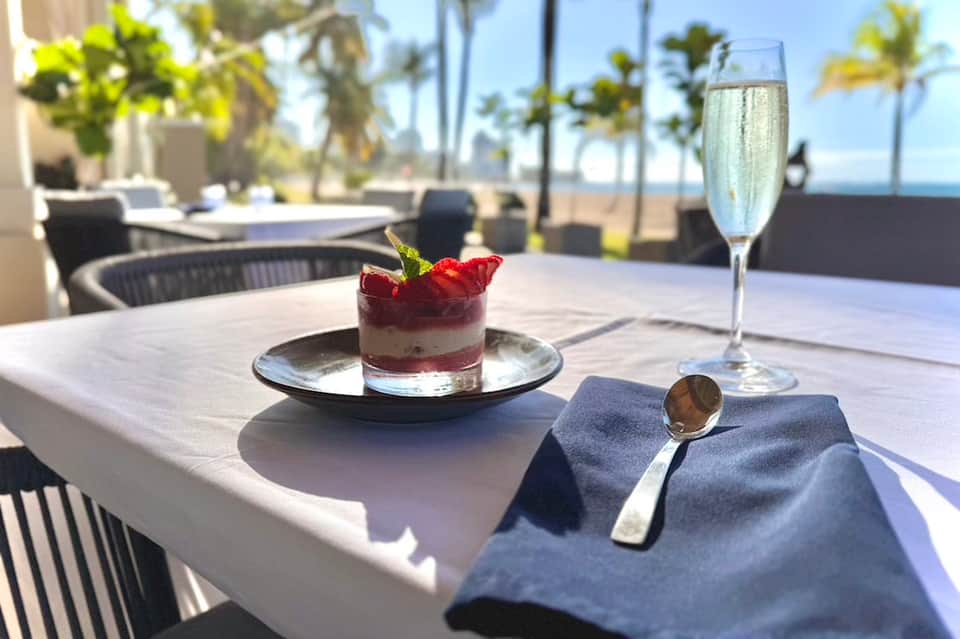 Fine dining dessert and champagne on table with beach and palm trees visible in background