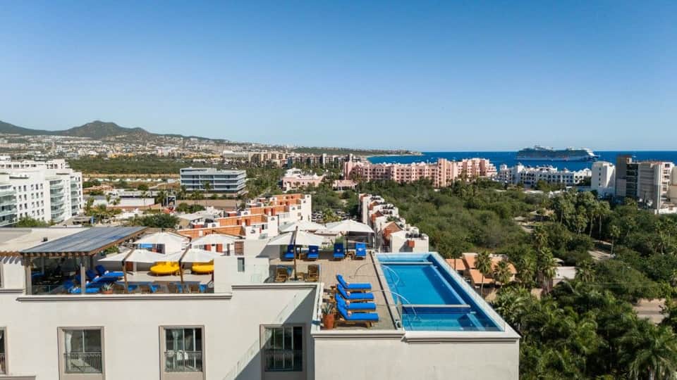 Rooftop pools and hot tubs overlooking coastal Mediterranean resort town with mountains and sea horizon view
