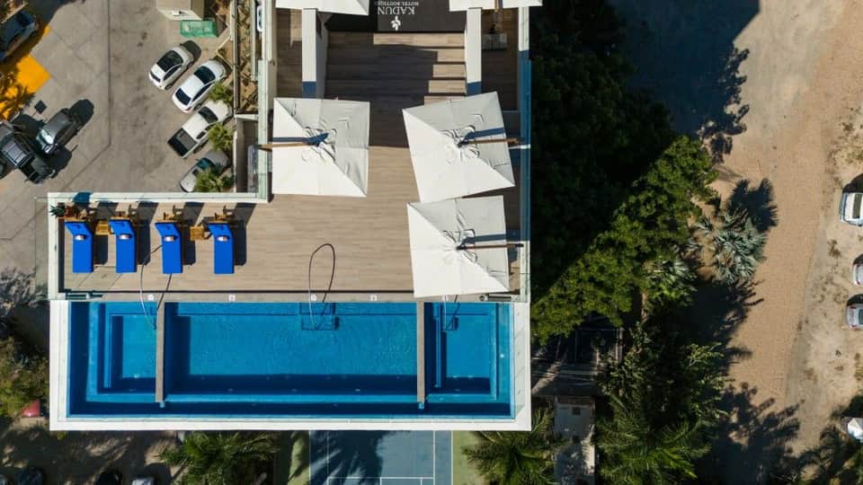 Aerial view of resort pool deck with blue pool, white umbrellas, sand beach, and ocean waterfront