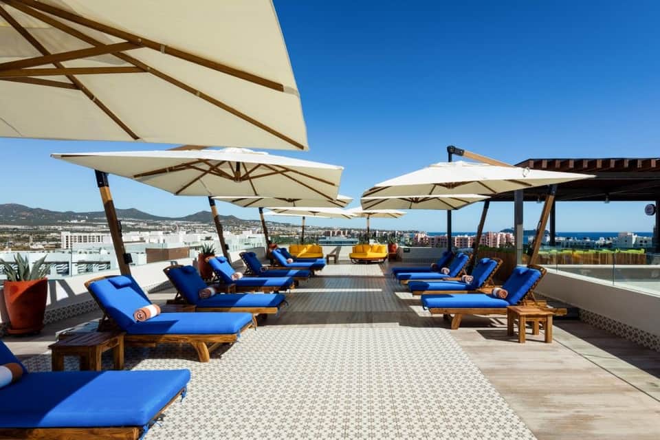 Rooftop lounge with lounge chairs, umbrellas, city skyline view, and modern landscape design