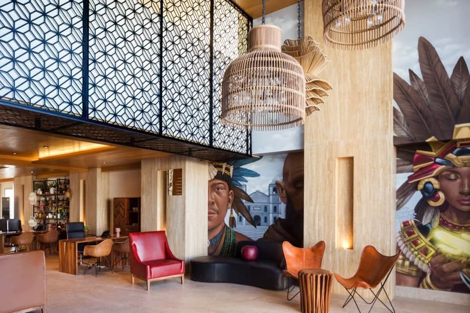 Modern hotel lobby with geometric wall panels, woven pendant lights, and colorful abstract murals