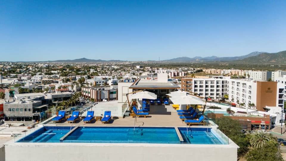 Rooftop pool overlooking city with blue loungers, mountains in distance, and modern buildings