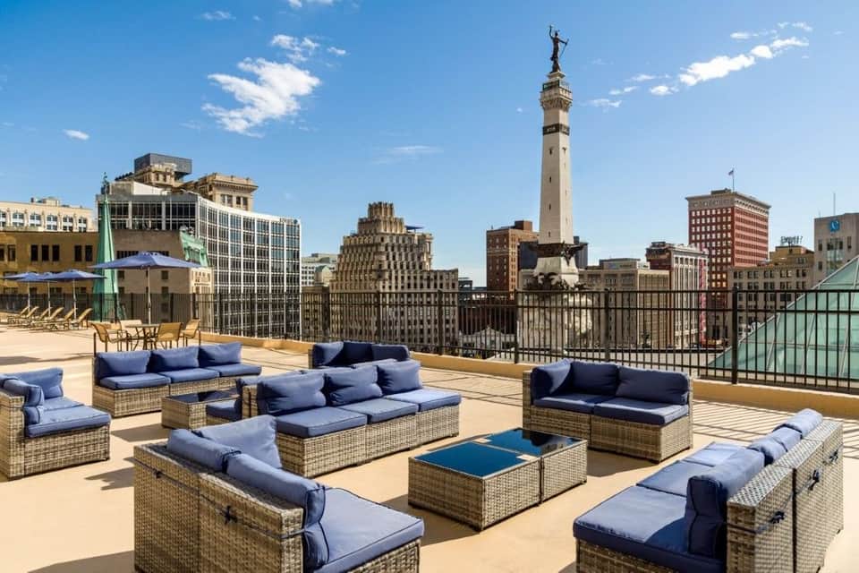 Rooftop lounge with wicker seating, blue cushions, city skyline views including historic buildings and monuments