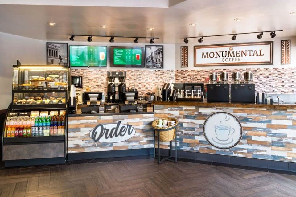 Bright coffee shop counter with Monumental Coffee signage, pastry display, menu boards, and service area