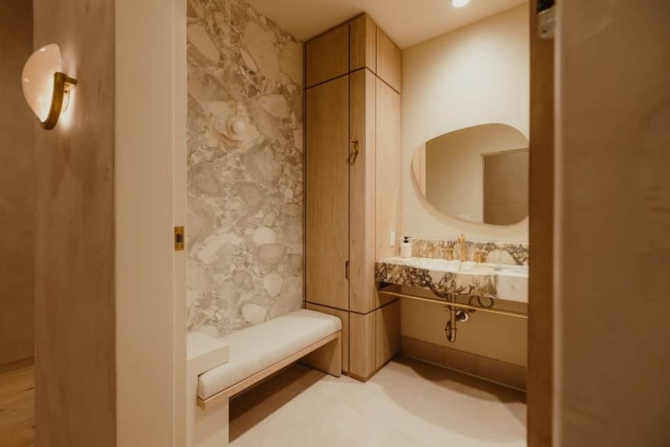 Modern luxury bathroom with marble shower, wooden vanity, and curved mirror with brass fixtures
