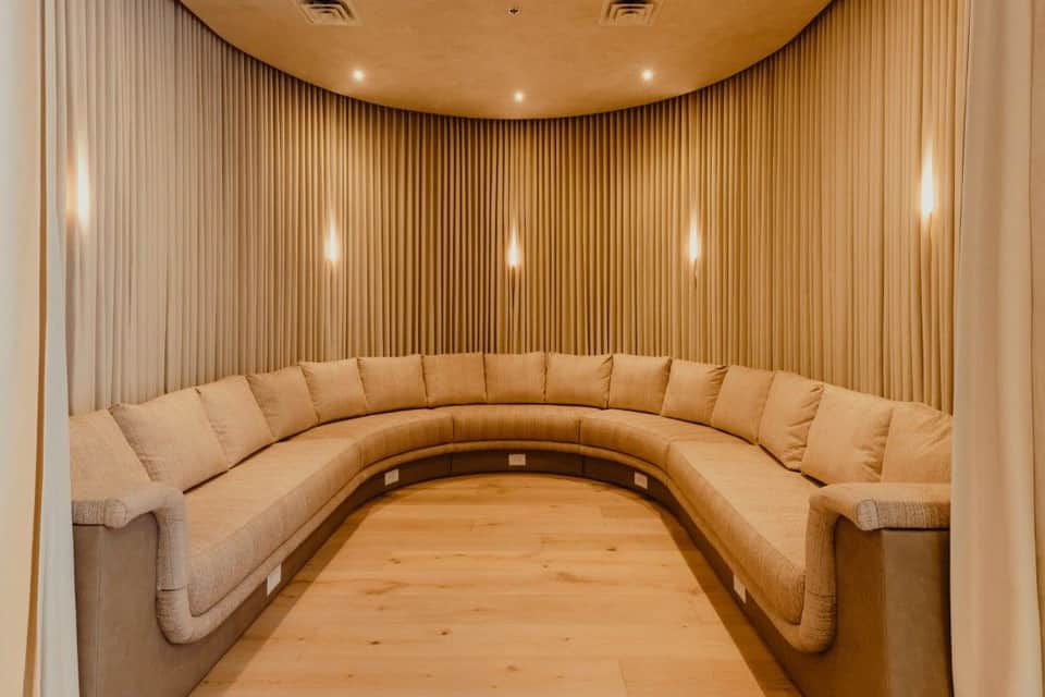 Curved cream-colored sectional sofa in modern curved room with vertical wood paneling and recessed lighting
