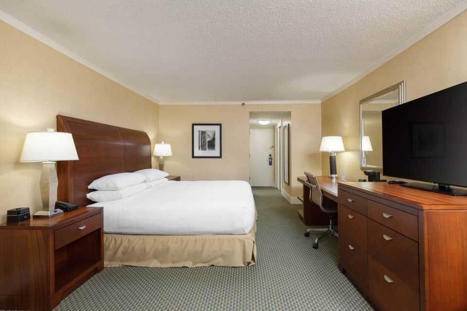 Hotel bedroom with wooden headboard, warm beige walls, flat-screen TV, and traditional furnishings