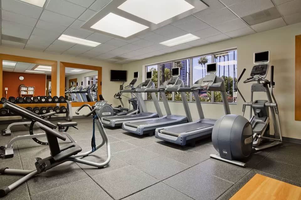 Hotel fitness center with treadmills, exercise bikes, dumbbells, and floor-to-ceiling windows