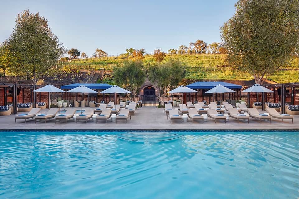 Vineyard pool area with lounge chairs, blue umbrellas, and scenic hillside views