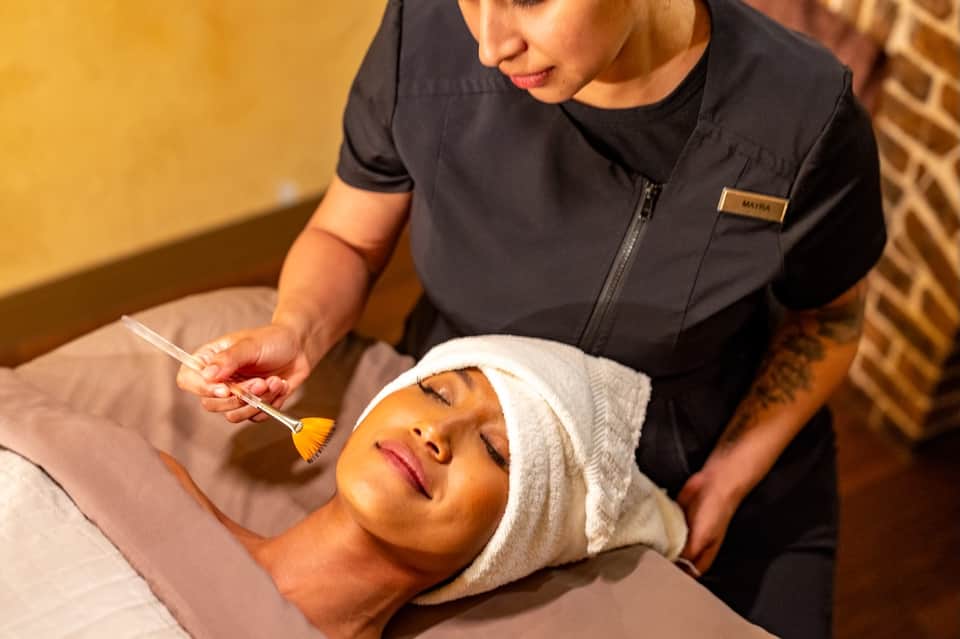 Spa therapist applying facial treatment to relaxed guest with headwrap and closed eyes