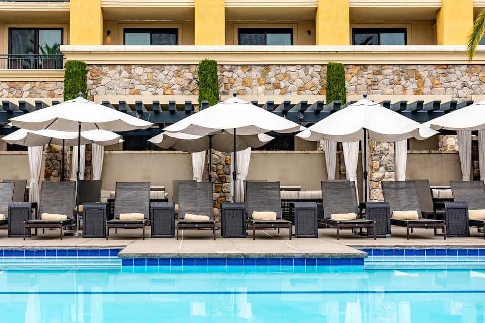 Resort pool with turquoise water, white umbrellas, cushioned lounge chairs, and stone accent wall