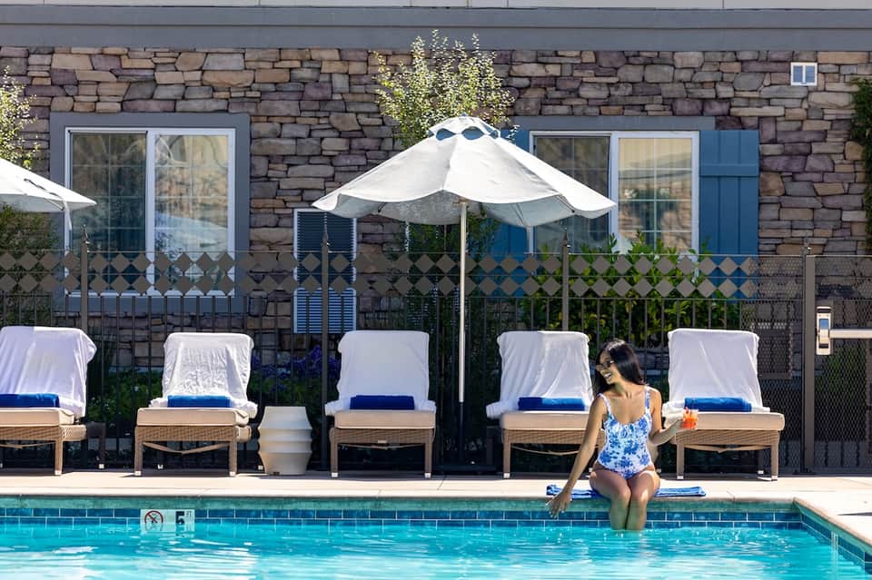 Resort pool with loungers under white umbrellas, stone building facade, and guest in water