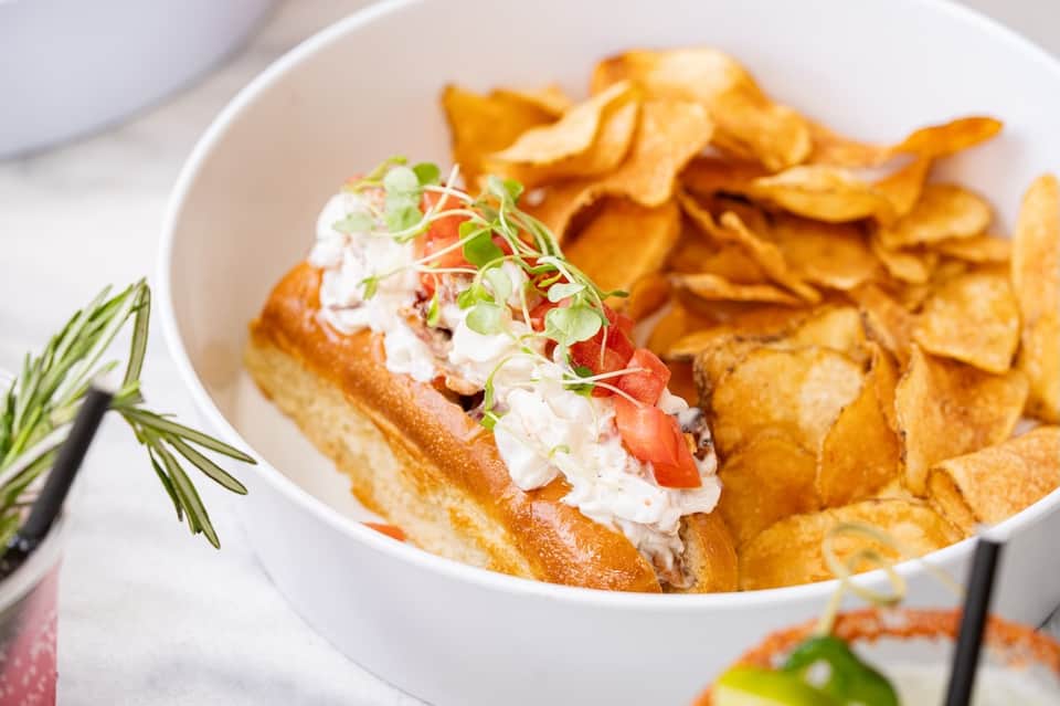Gourmet lobster roll sandwich with crispy potato chips on white plate