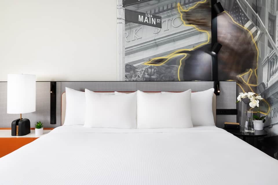 Contemporary hotel bedroom with white bedding, black headboard, urban street art mural, and modern minimalist design