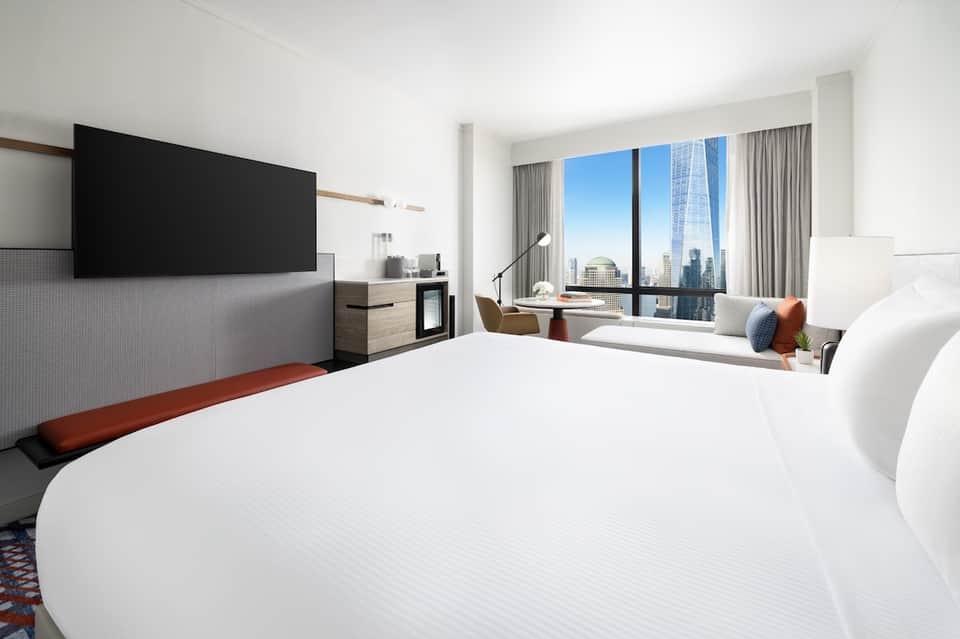 Modern high-rise hotel bedroom with city skyline view through floor-to-ceiling windows and contemporary furnishings