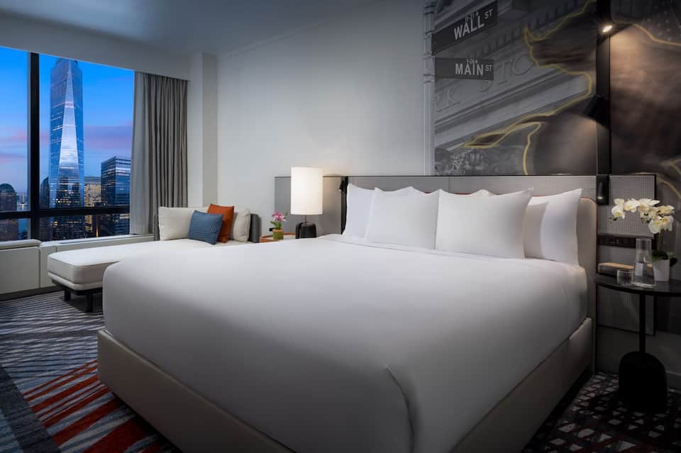 Luxury hotel bedroom with city skyline view, white bedding, and modern furnishings
