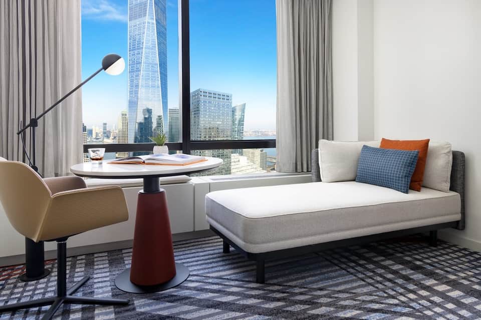 Modern hotel room with city skyline views through floor-to-ceiling windows and contemporary furnishings