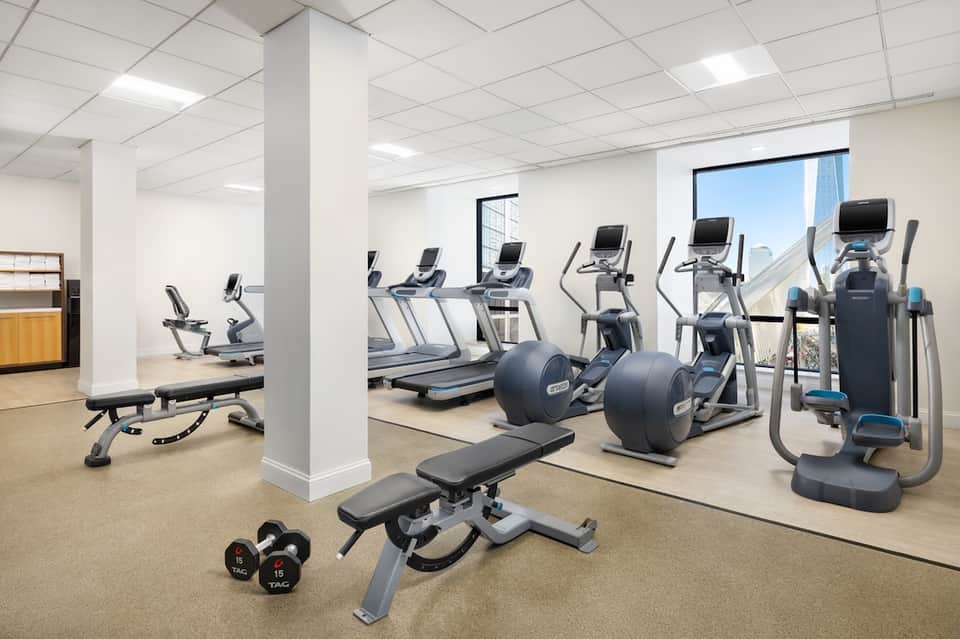 Modern fitness center with cardio equipment, free weights, treadmills, and floor-to-ceiling windows with city view