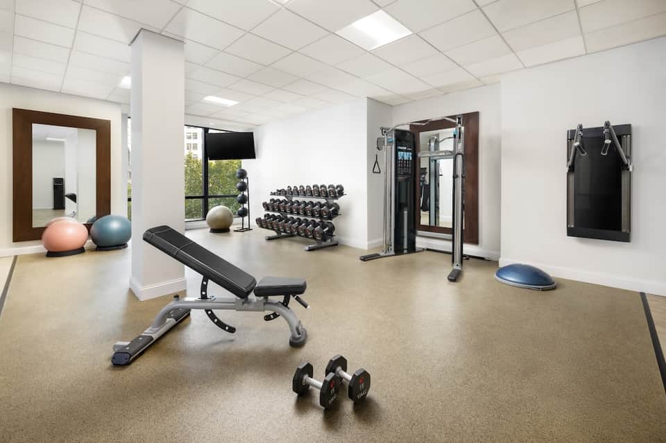 Fitness center with cardio equipment, free weights, mirrors, and exercise balls on light-colored floor