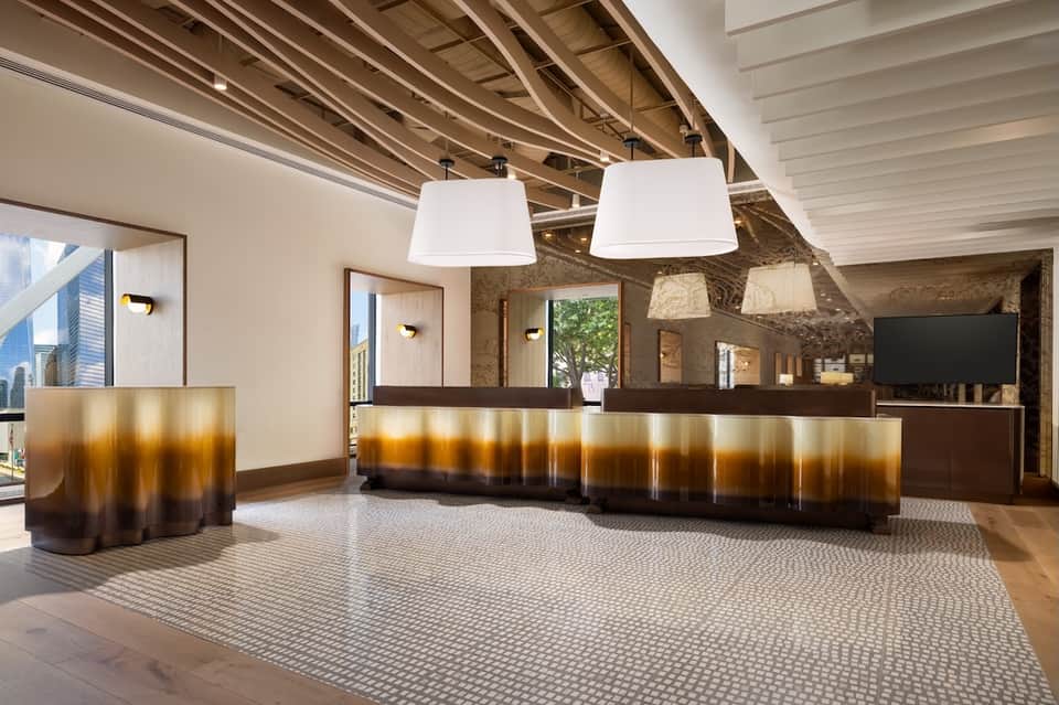 Modern hotel lobby with geometric patterned floor, artistic metallic desk, and white pendant lights