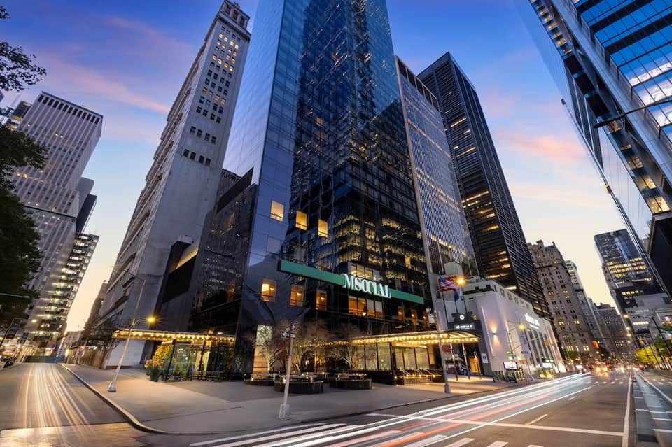 Modern glass and steel downtown office or hotel tower illuminated at dusk with street-level retail entrance