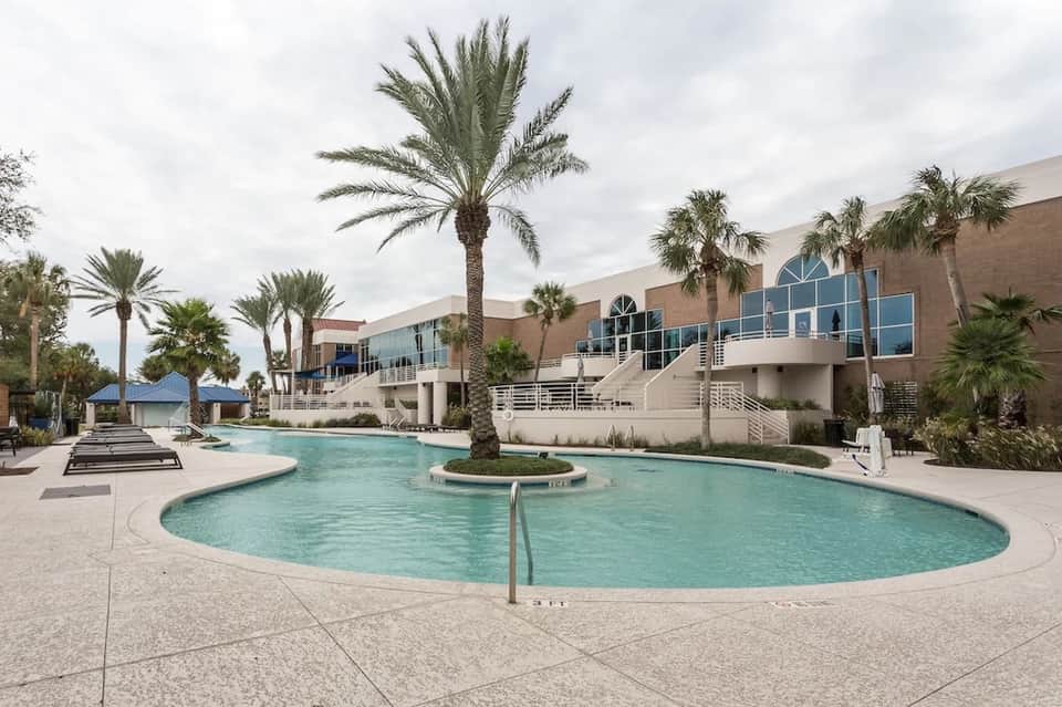 Large circular resort pool surrounded by palm trees and modern building with blue windows